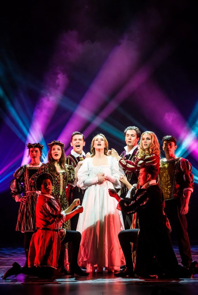 Cast of Six the Musical performing under colorful lighting