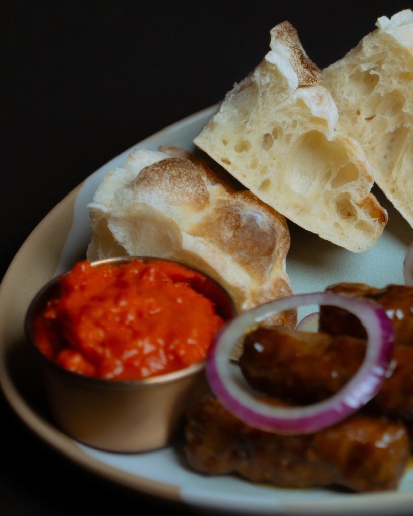 AMARA Chicago ćevapi with ajvar and torn somun bread on a plate