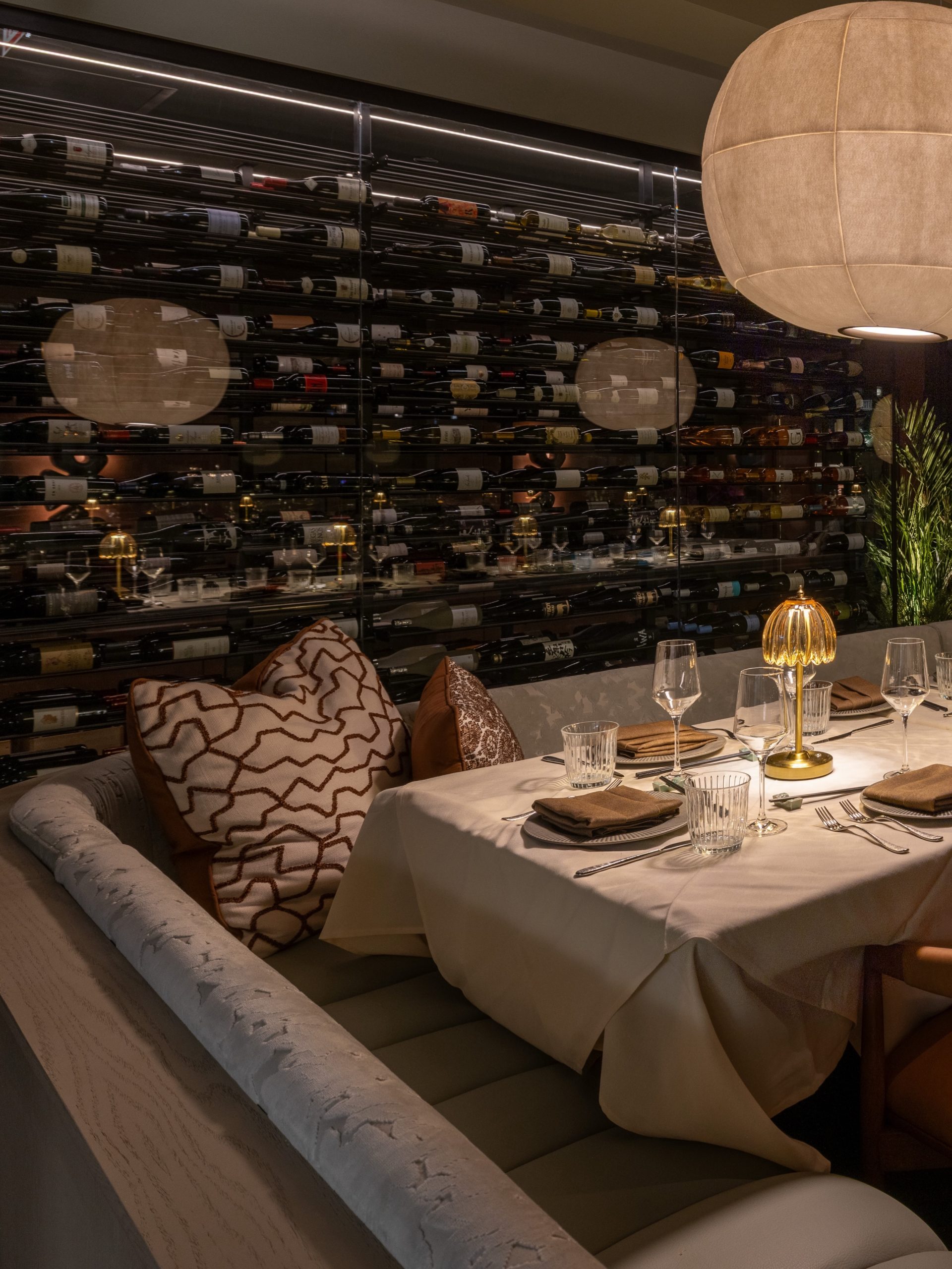 Arla Chicago banquette table set beside floor-to-ceiling glass wine wall
