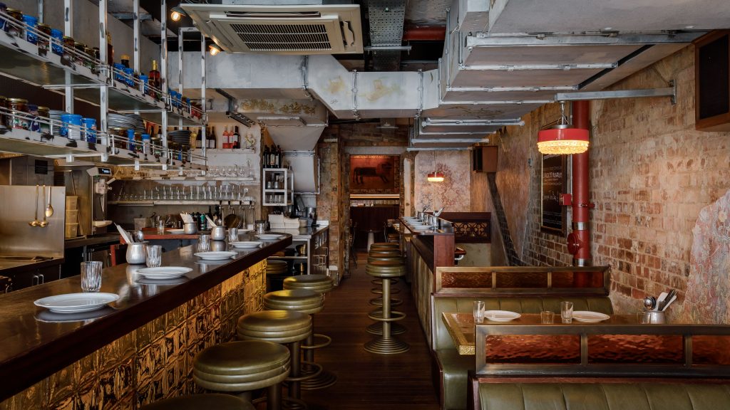 Berenjak restaurant interior with bar, green leather stools, and booth seating