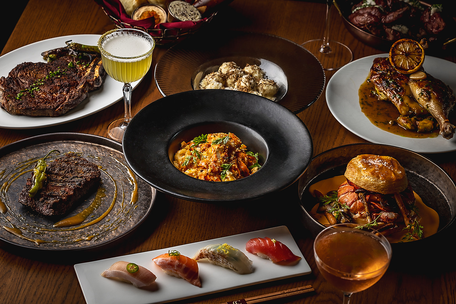 Carlyle Club Chicago steak, nigiri, lobster, and cocktails spread on a dark wood table