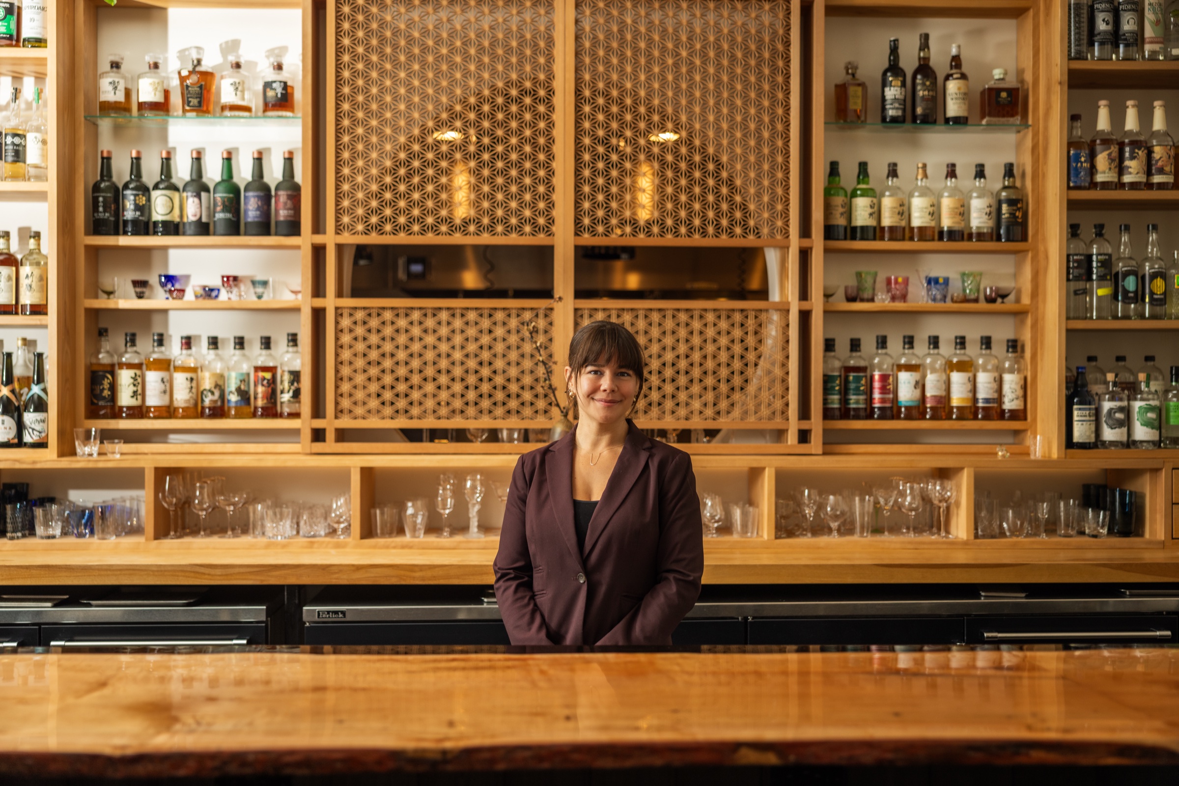 Julia Momosé behind the bar at Kumiko Chicago with bottles, glassware, and kumiko wood screen