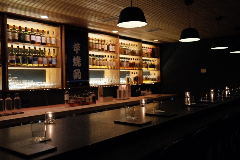 Kumiko Chicago whisky bar with backlit bottles, bar rail, candles, and pendant lights