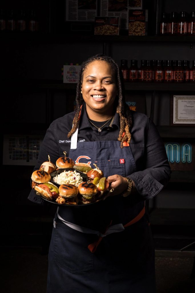 Chef Dominique Leach of Lexington Betty Smokehouse holding a platter of BBQ sliders with coleslaw and pickles