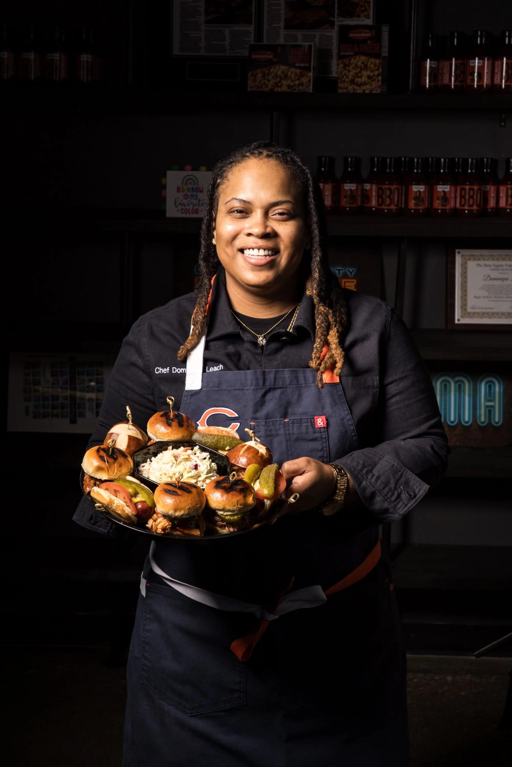 Chef Dominique Leach of Lexington Betty Smokehouse holding a platter of BBQ sliders with coleslaw and pickles