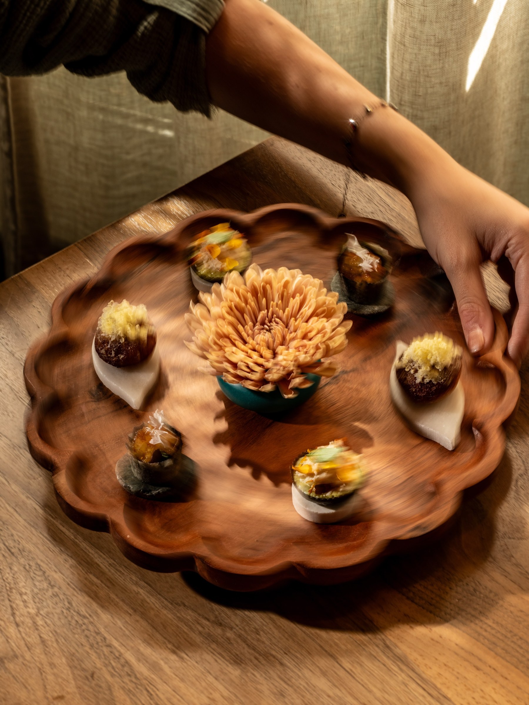 A scalloped wooden platter of first-course bites set on a table at All Well Chicago