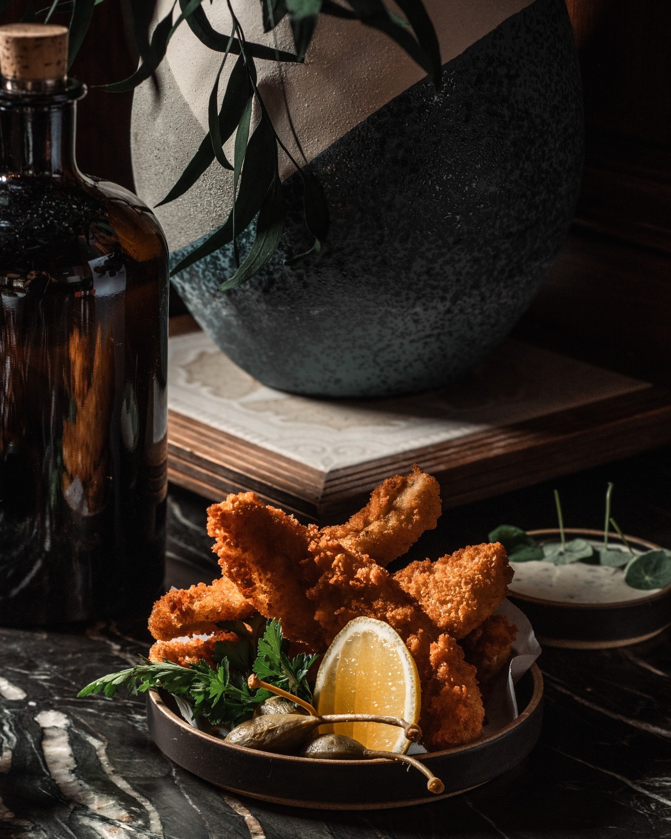 Fried lake perch with lemon and tartar sauce on a dark marble bar at All Well Chicago