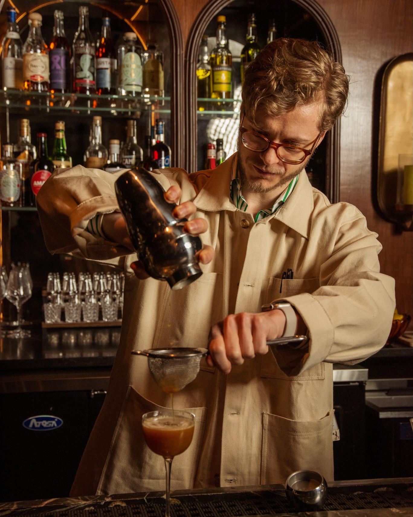 Bar director Maxx Kleiner straining a cocktail behind the bar at All Well Chicago