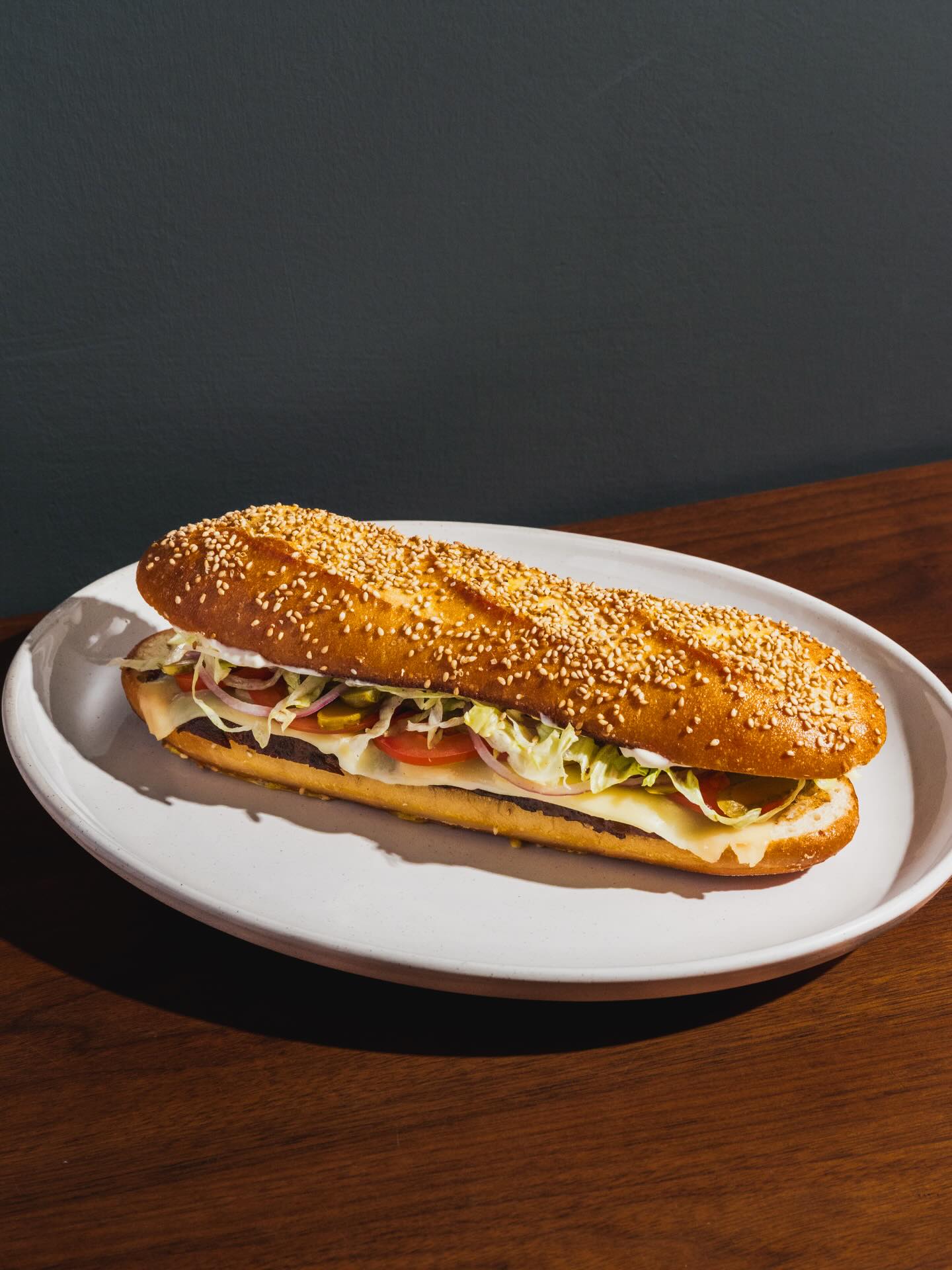Short rib sandwich on a sesame roll with pickles on a white plate at All Well Chicago