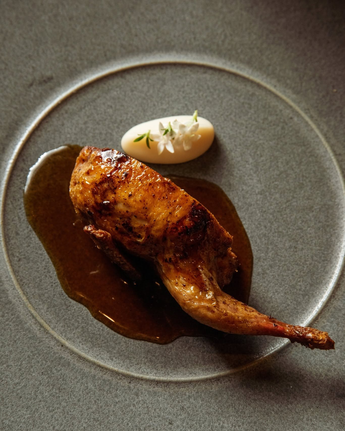Glazed truffle stuffed quail in a pool of sauce on a gray plate at All Well Chicago