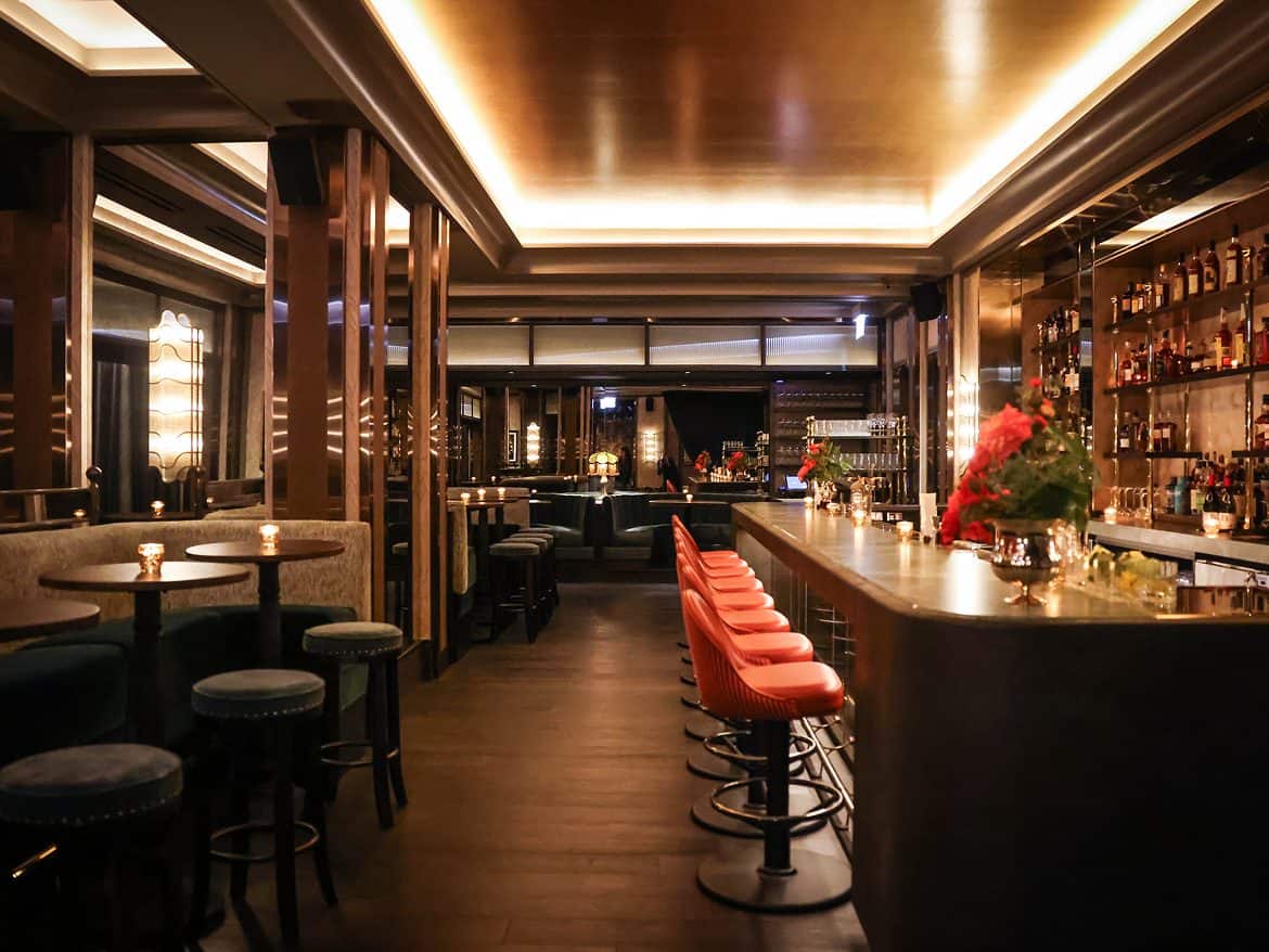 Bar lounge with orange stools and backlit bottles at The Alston Chicago