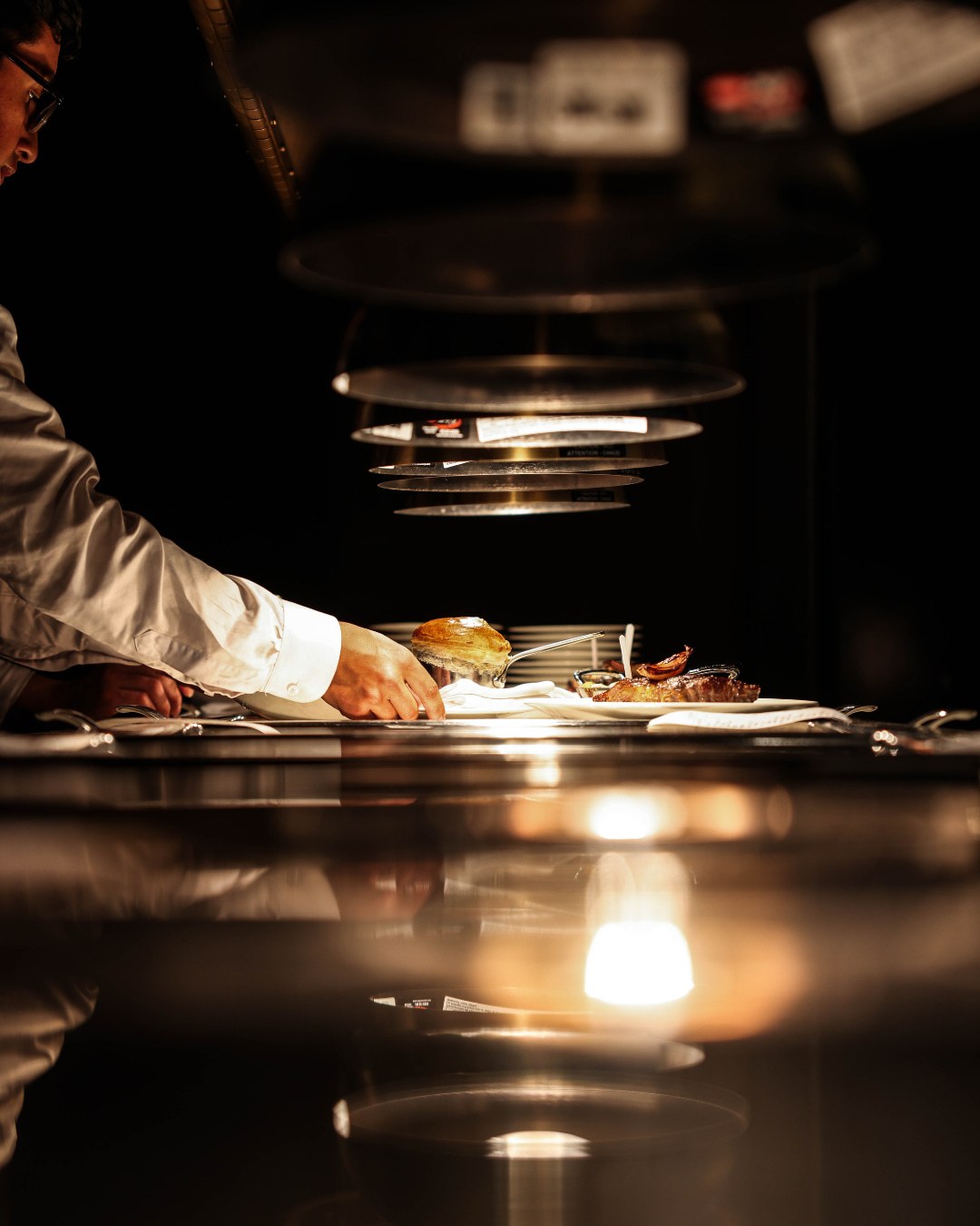 Chef plating at the kitchen pass under heat lamps at The Alston Chicago