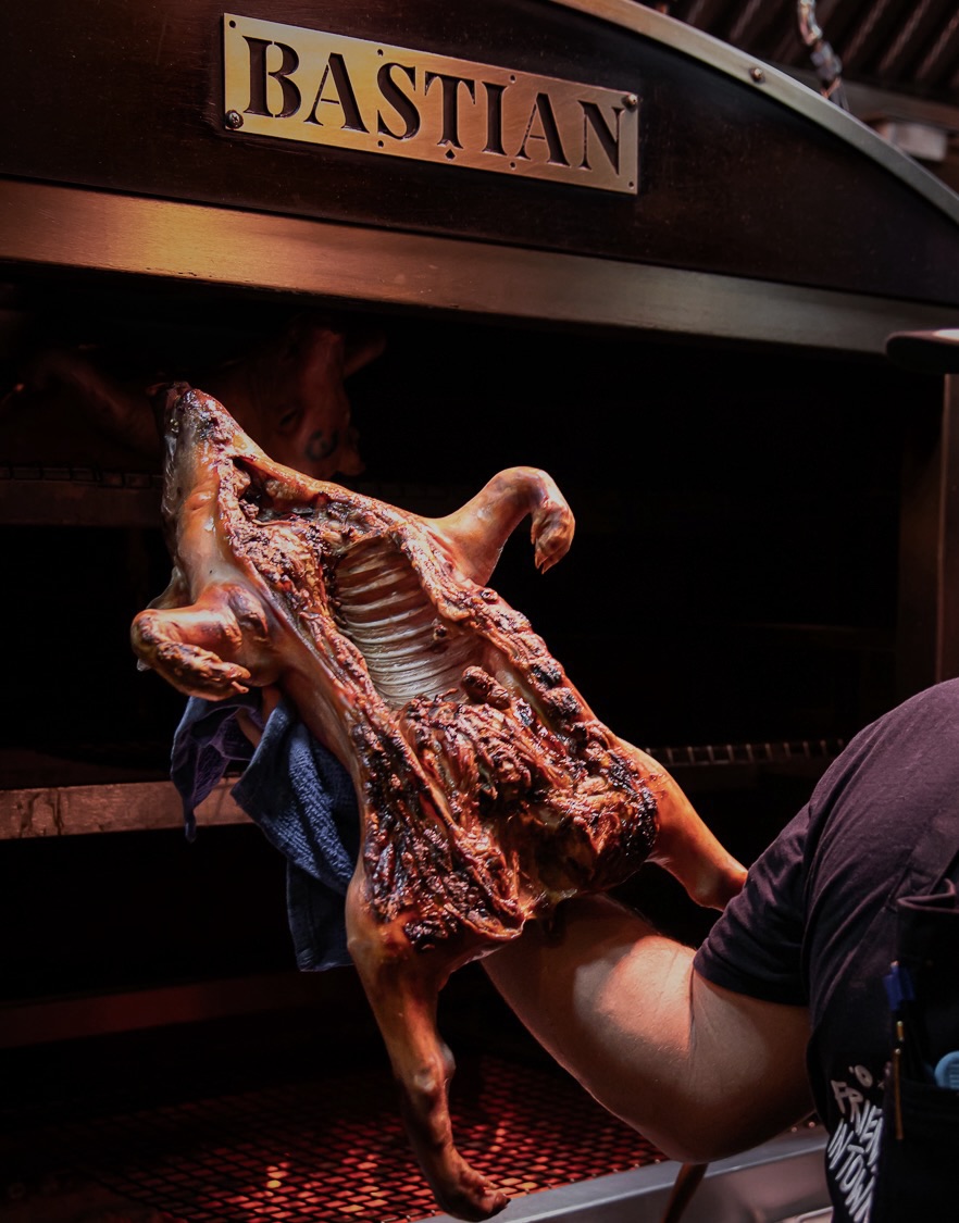 A cook carries a whole Segovian pig in front of the Bastian sign at Asador Bastian in Chicago