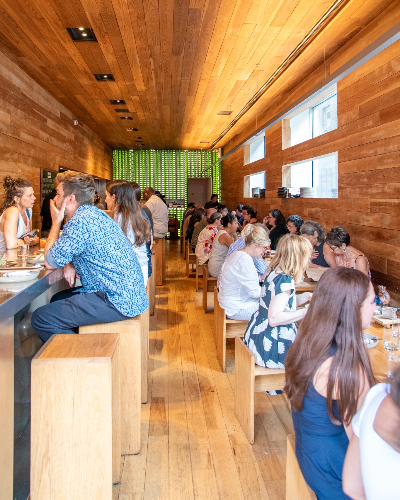 Diners fill the long cedar communal tables and counter seats in the wood-paneled dining room at avec West Loop