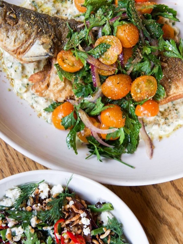 Whole roasted branzino with sungold tomatoes and herbs next to a green bean and plum tabbouleh