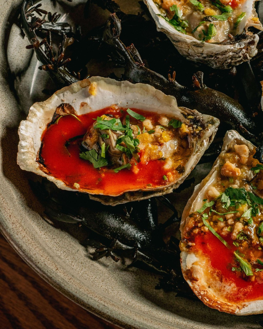 Grilled oysters in red chile butter topped with crumbs and herbs on a stoneware plate