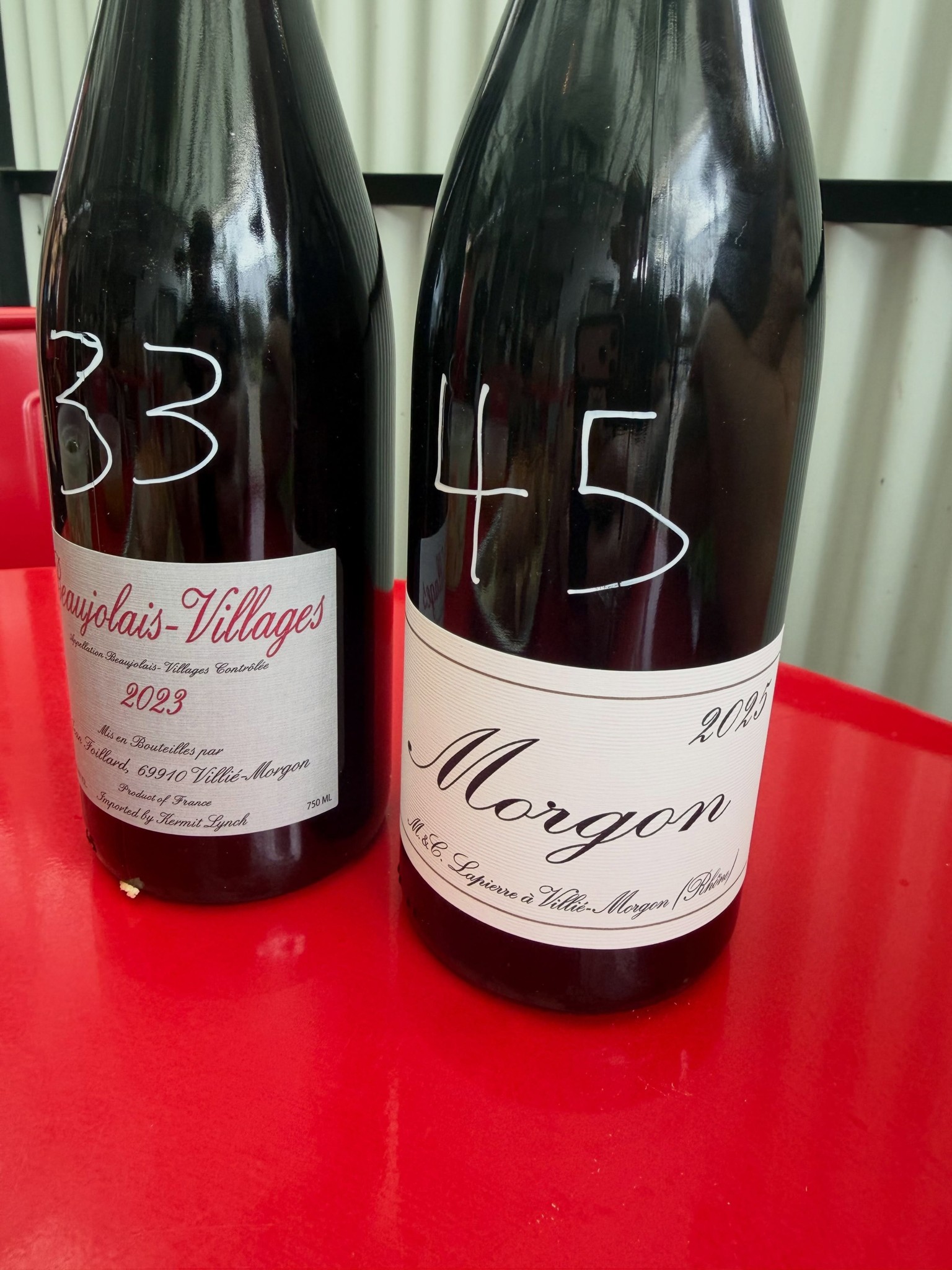 Bottles of Beaujolais-Villages and Morgon with prices written on the labels on a red table at Chez Poulet Chicago