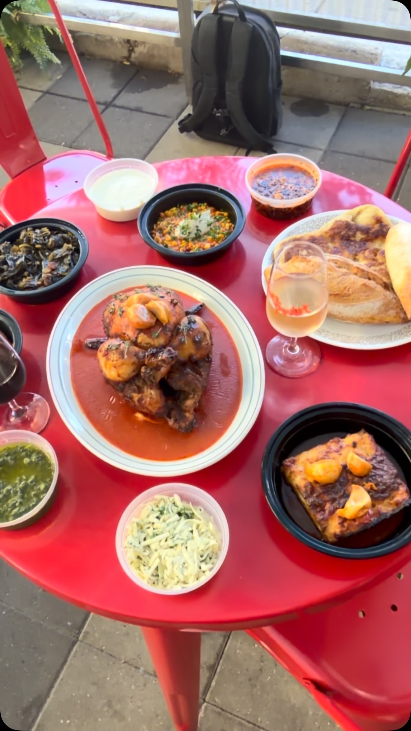 A red patio table with rotisserie chicken in jus, macaroni gratin, collards, sauces and a glass of rosé at Chez Poulet Chicago