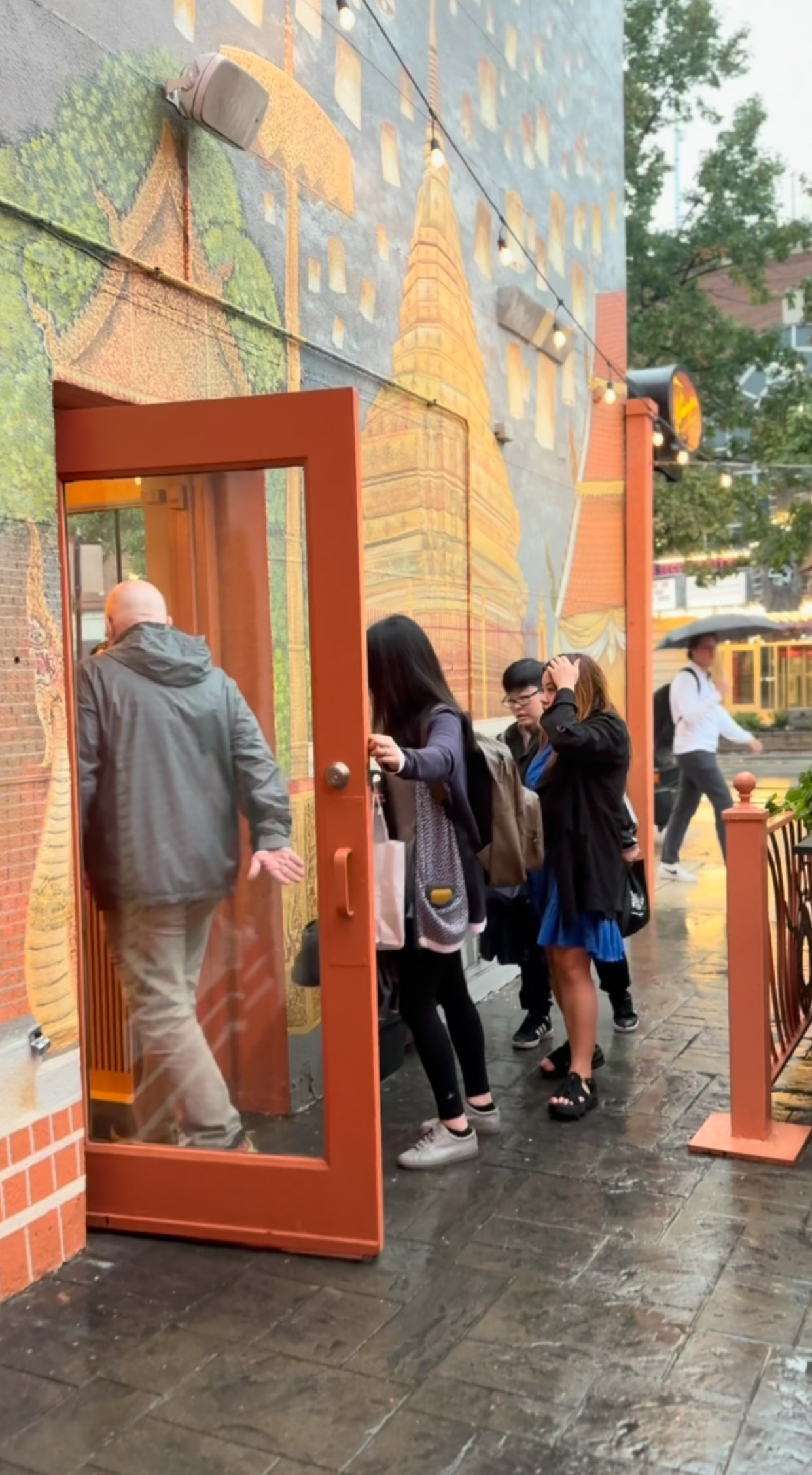 Guests walking into Chiang Mai Night Bazaar through the orange front door beside the temple mural in Old Town
