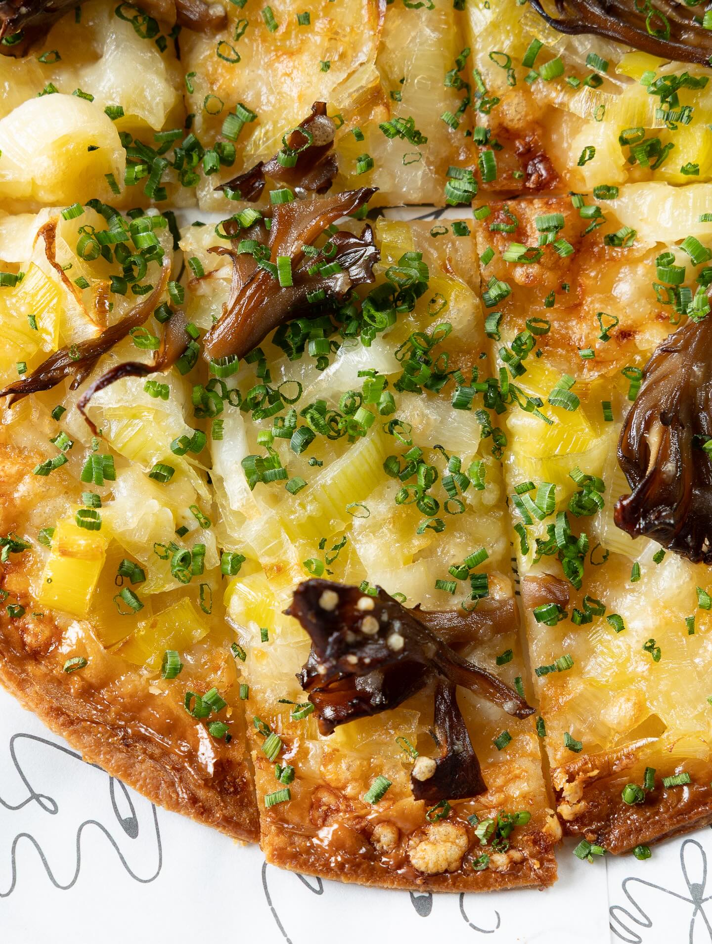 Tavern-style tarte flambe cut into squares, topped with onions, smoked maitake mushrooms and chives