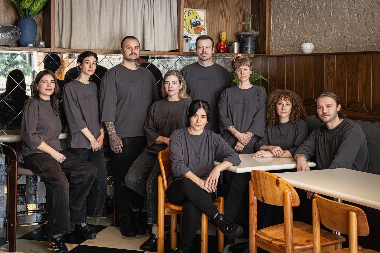 The Creepies team in gray uniforms stands among wood chairs and tables in the paneled dining room