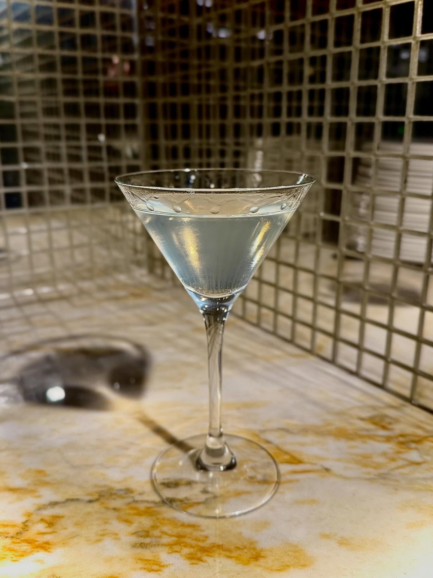 A Vesper martini in a stemmed glass on a marble ledge in front of gold mosaic tile