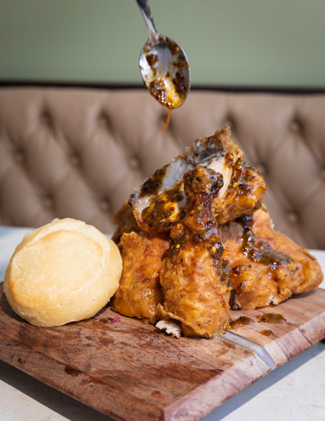 Double crispy fried chicken glazed with chili crisp honey butter next to a round of cornbread on a wooden board