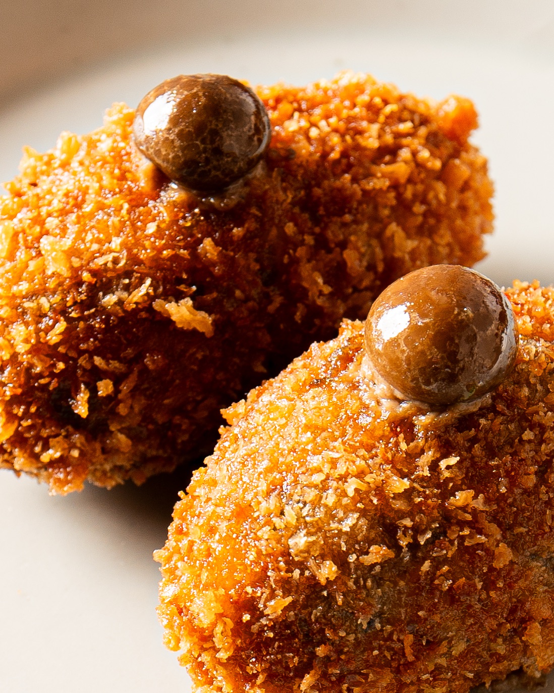Two golden adobo mushroom croquetas topped with glazed mushroom caps at Donia in London