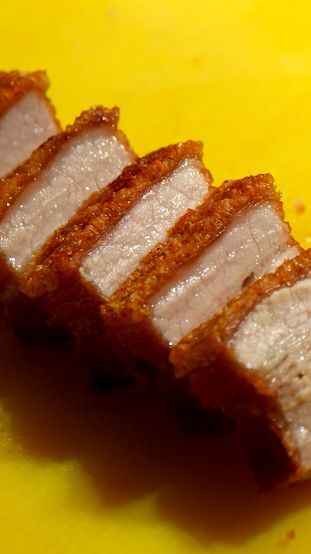 Slices of crispy lechon pork belly with blistered skin against a bright yellow background at Donia