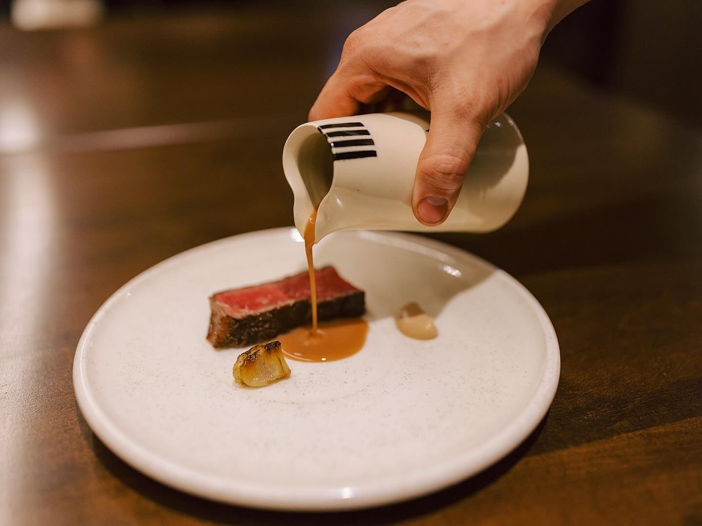 Aged beef jus poured over dry-aged ribeye and grilled cipollini at Feld Chicago