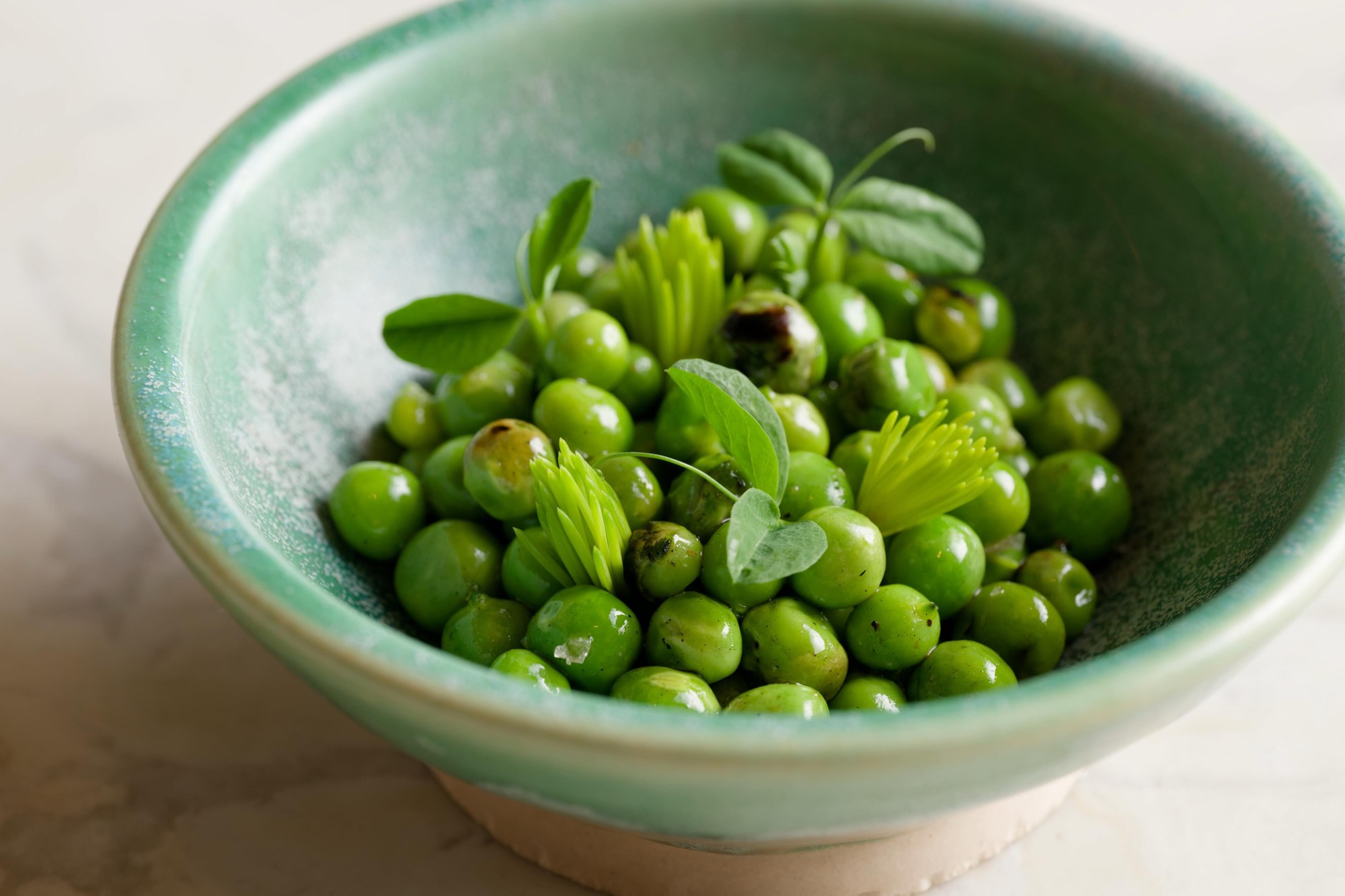 Grilled peas with goat butter, spruce tips and pea shoots in a green bowl at Feld Chicago