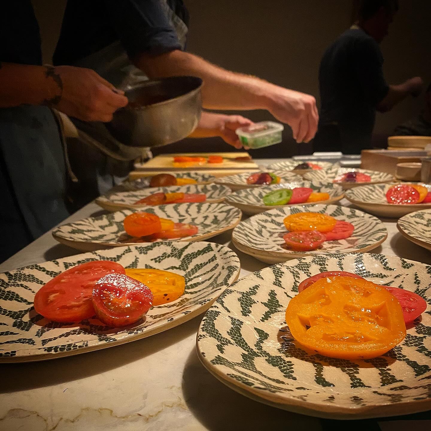 Heirloom tomato courses plated on patterned ceramic plates on the pass at Feld Chicago