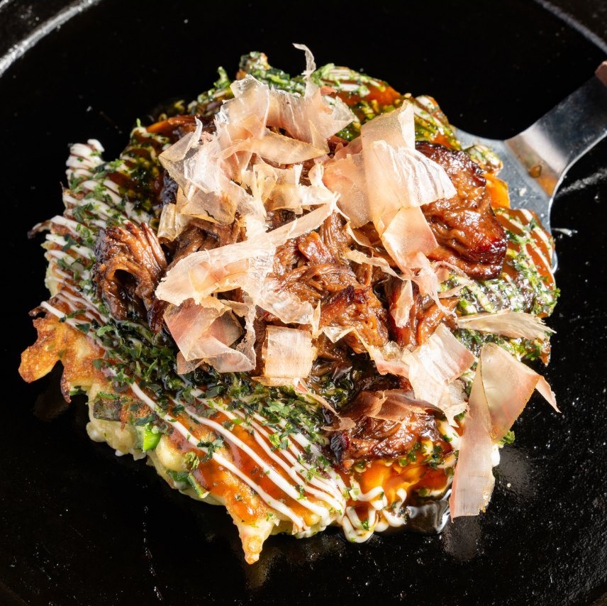 Braised wagyu beef cheek okonomiyaki piled with bonito flakes and striped with mayo