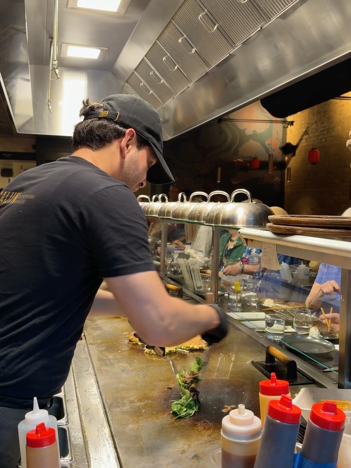 A cook works the long okonomiyaki griddle in front of diners at the chef's counter at Gaijin
