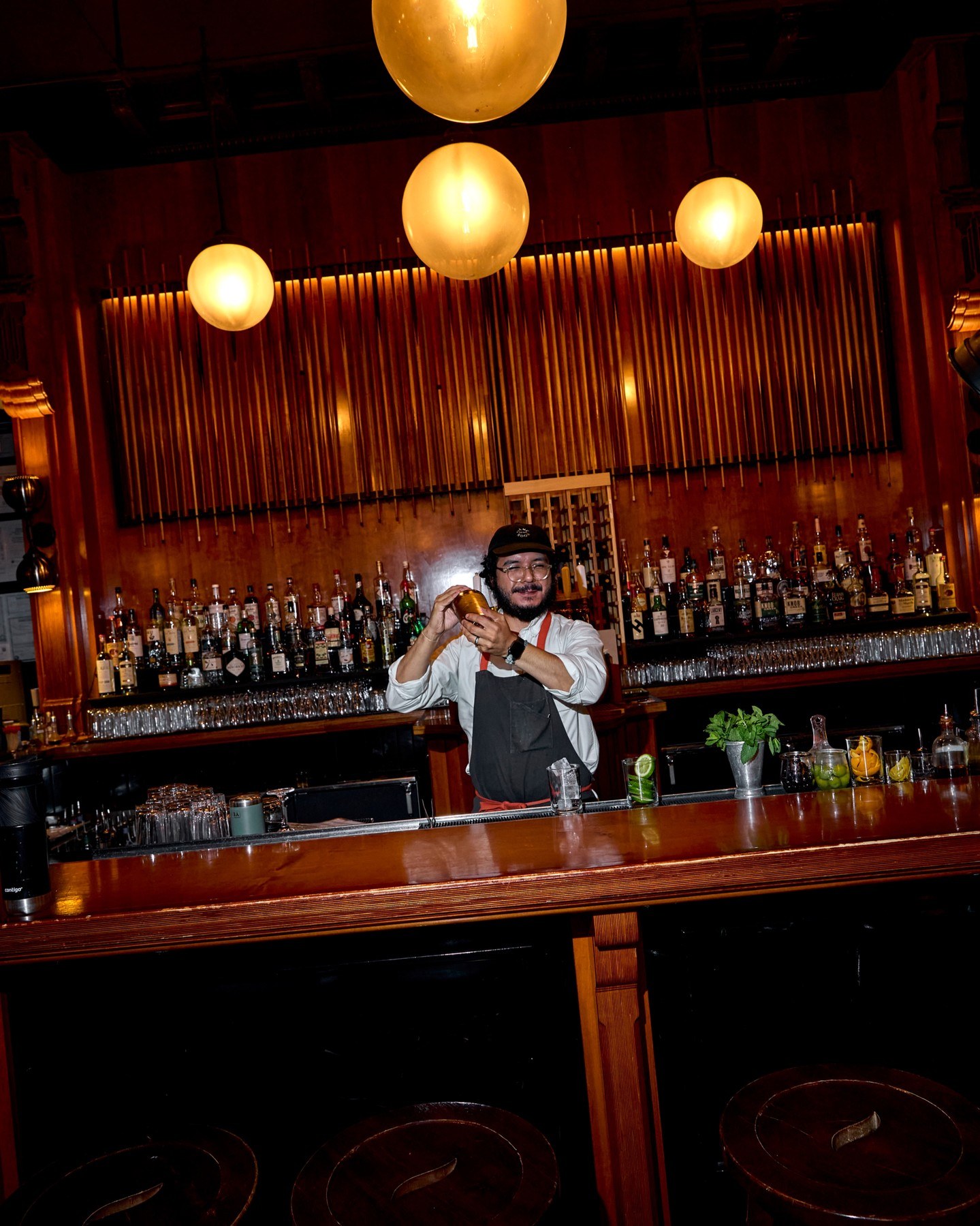 A bartender shaking a cocktail under globe lights at the wood-paneled Game Room bar