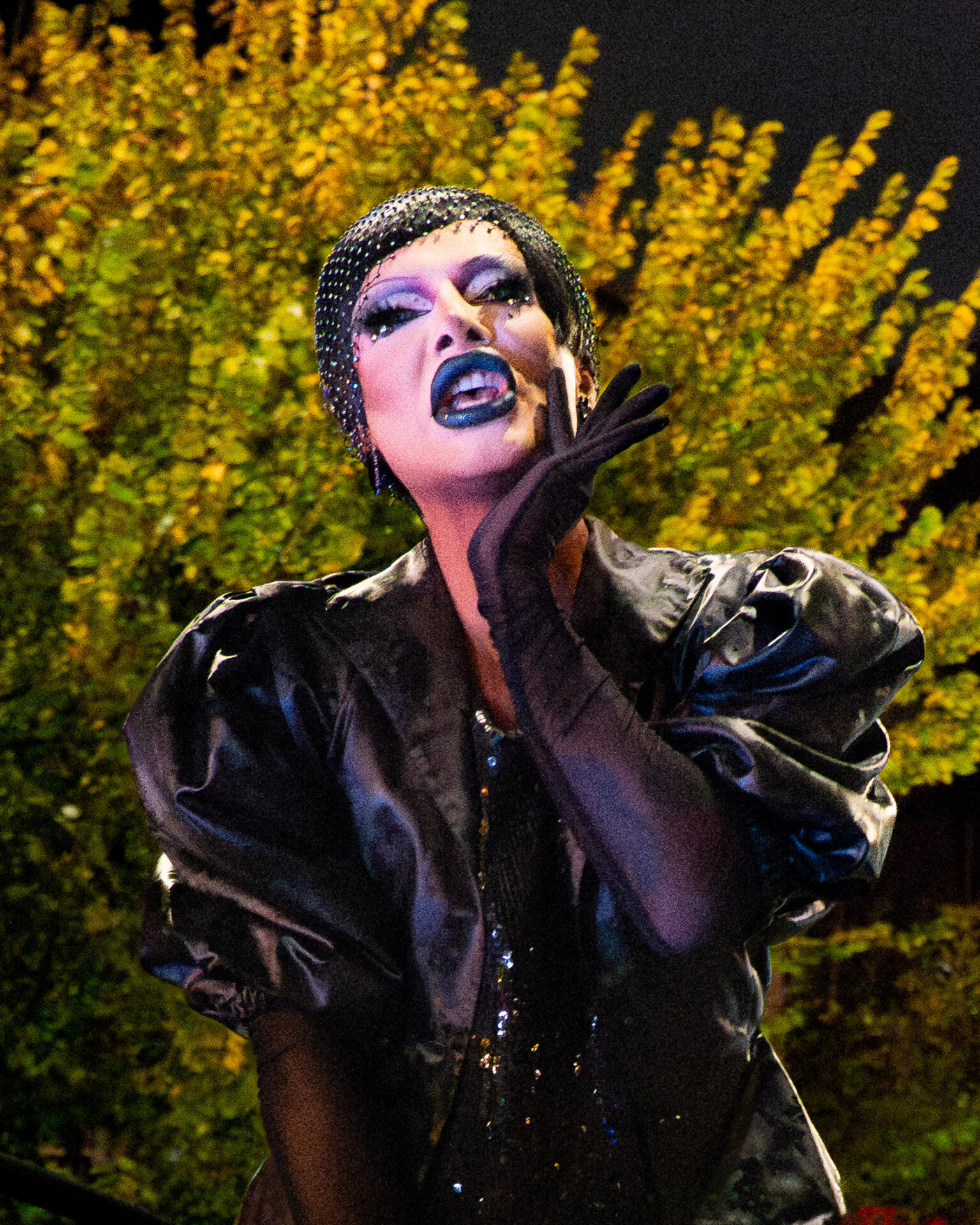 A drag performer in black latex and dramatic makeup poses on Halsted Street at Chicago's Haunted Halsted Halloween Parade