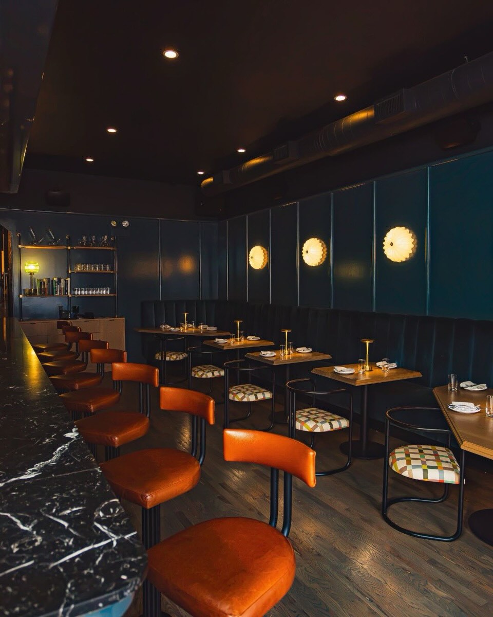 The dining room at Hooligan Chicago with dark blue walls, a blue velvet banquette, a long bar and orange leather stools