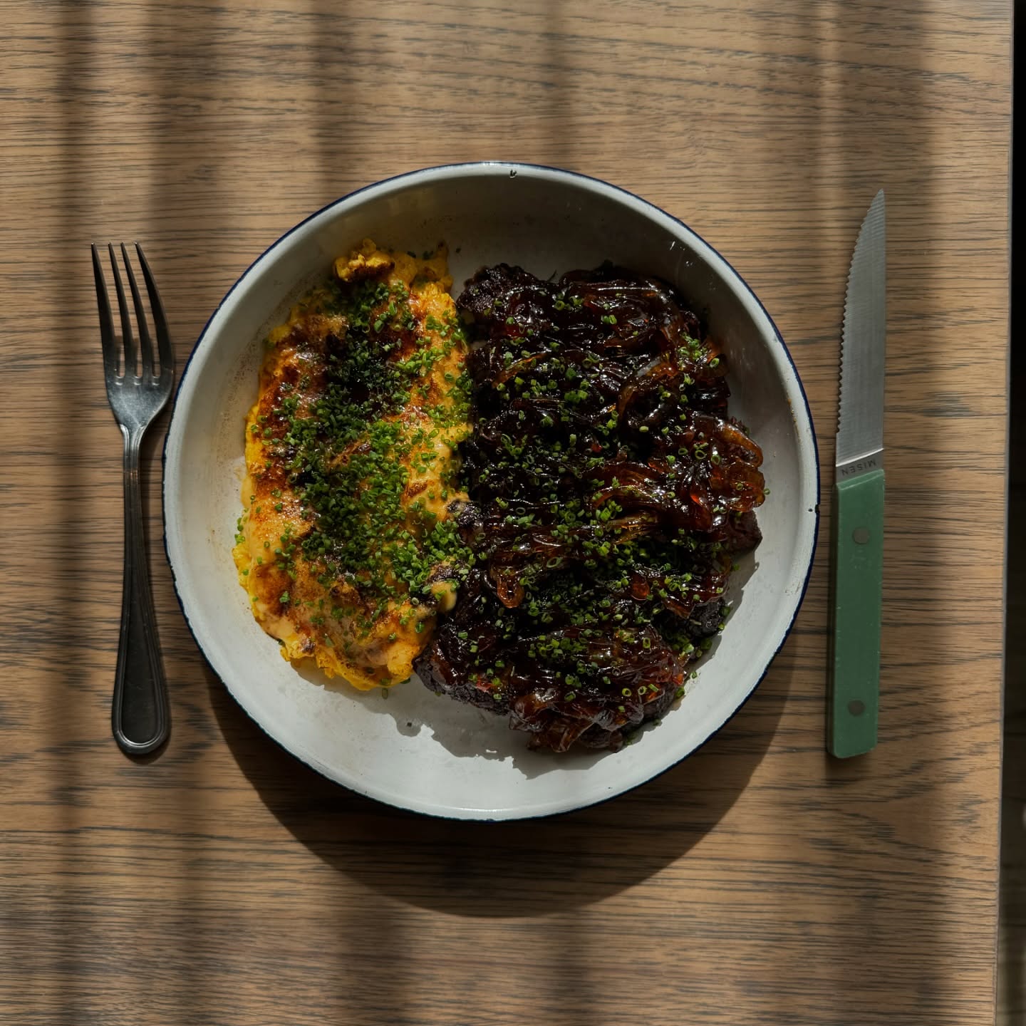 Overhead view of sliced wagyu ribeye with calamansi onion jam beside scrambled eggs on a plate at Kasama