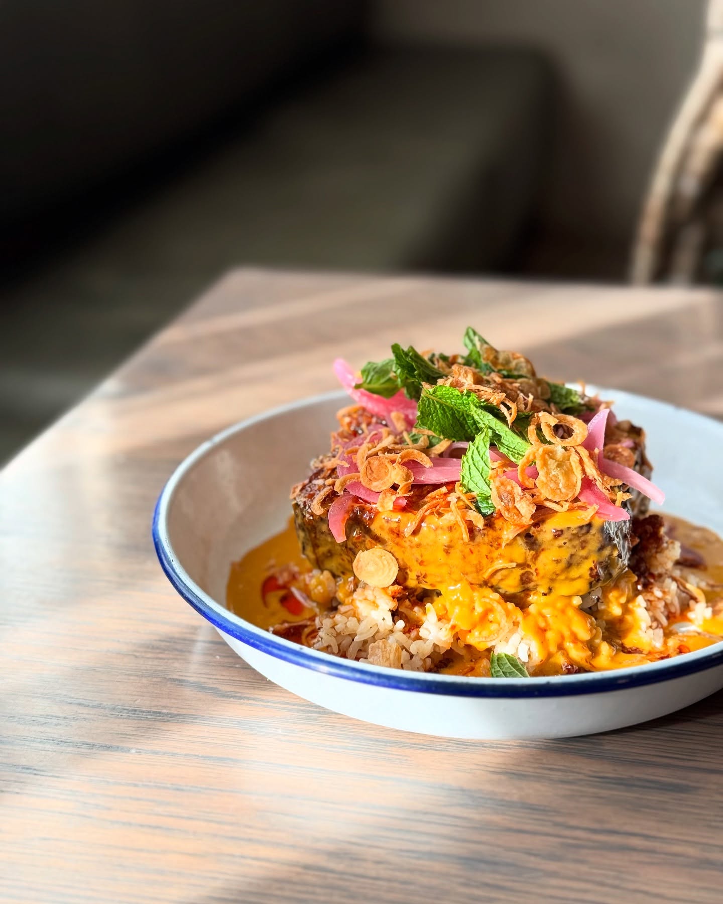 Kasama's kare-kare meatloaf in a white bowl, glossy peanut sauce under shrimp paste chili crisp, pickled onions and fried shallots