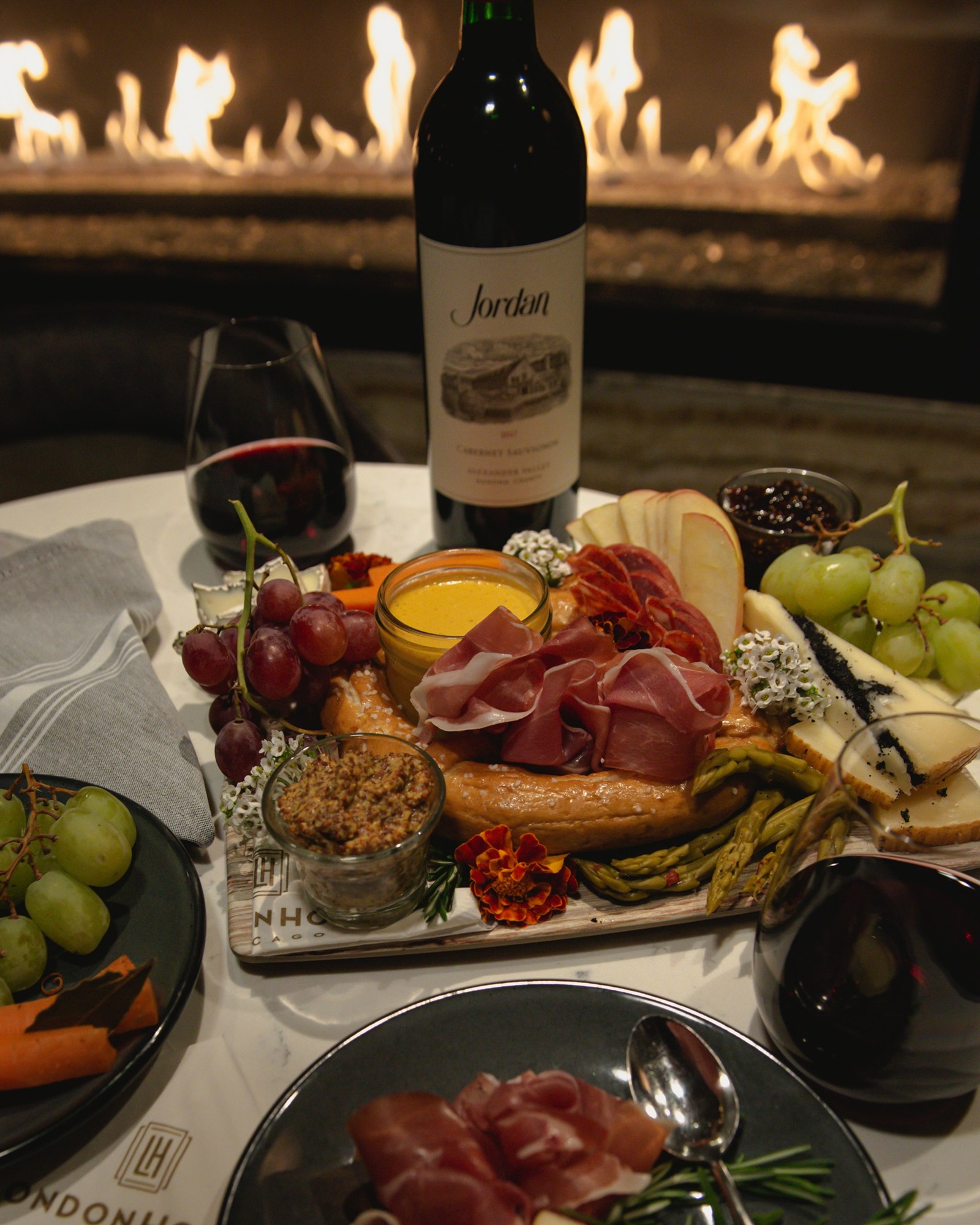 A pretzel and charcuterie board with red wine in front of a fireplace at LondonHouse Chicago