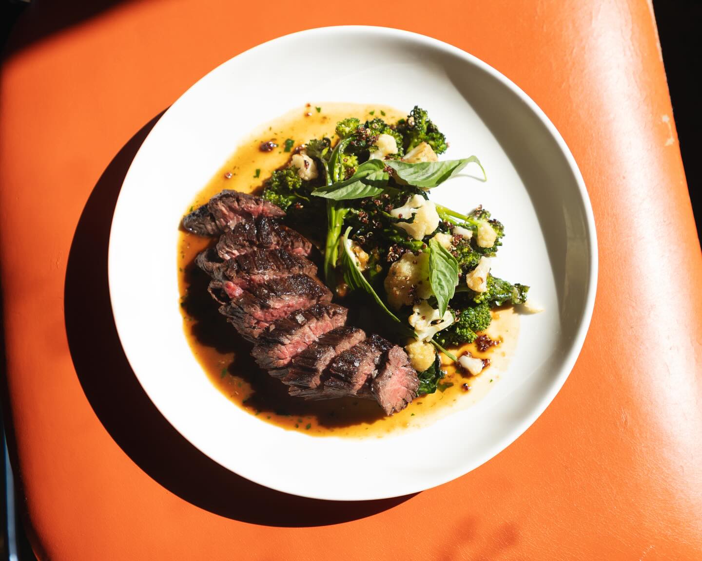 Sliced bavette steak with brassicas, basil and crispy grains on a white plate at Lula Cafe