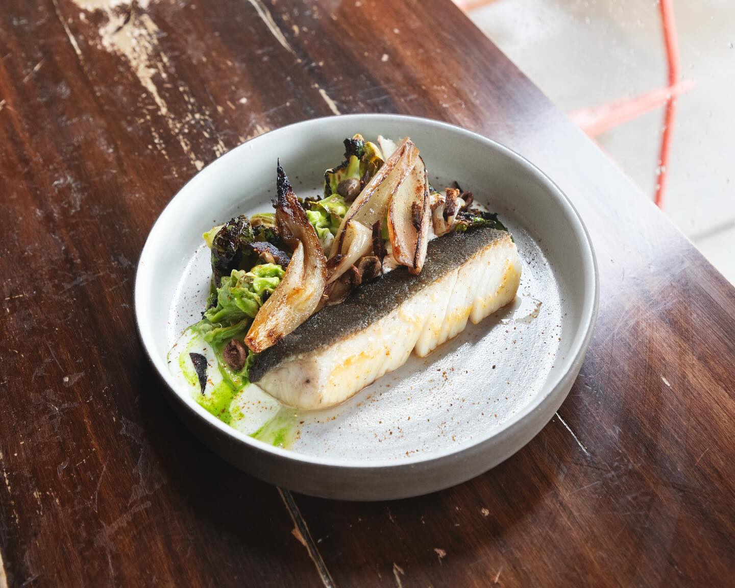 Seared black cod over savoy cabbage with olives and onions on a white plate at Lula Cafe