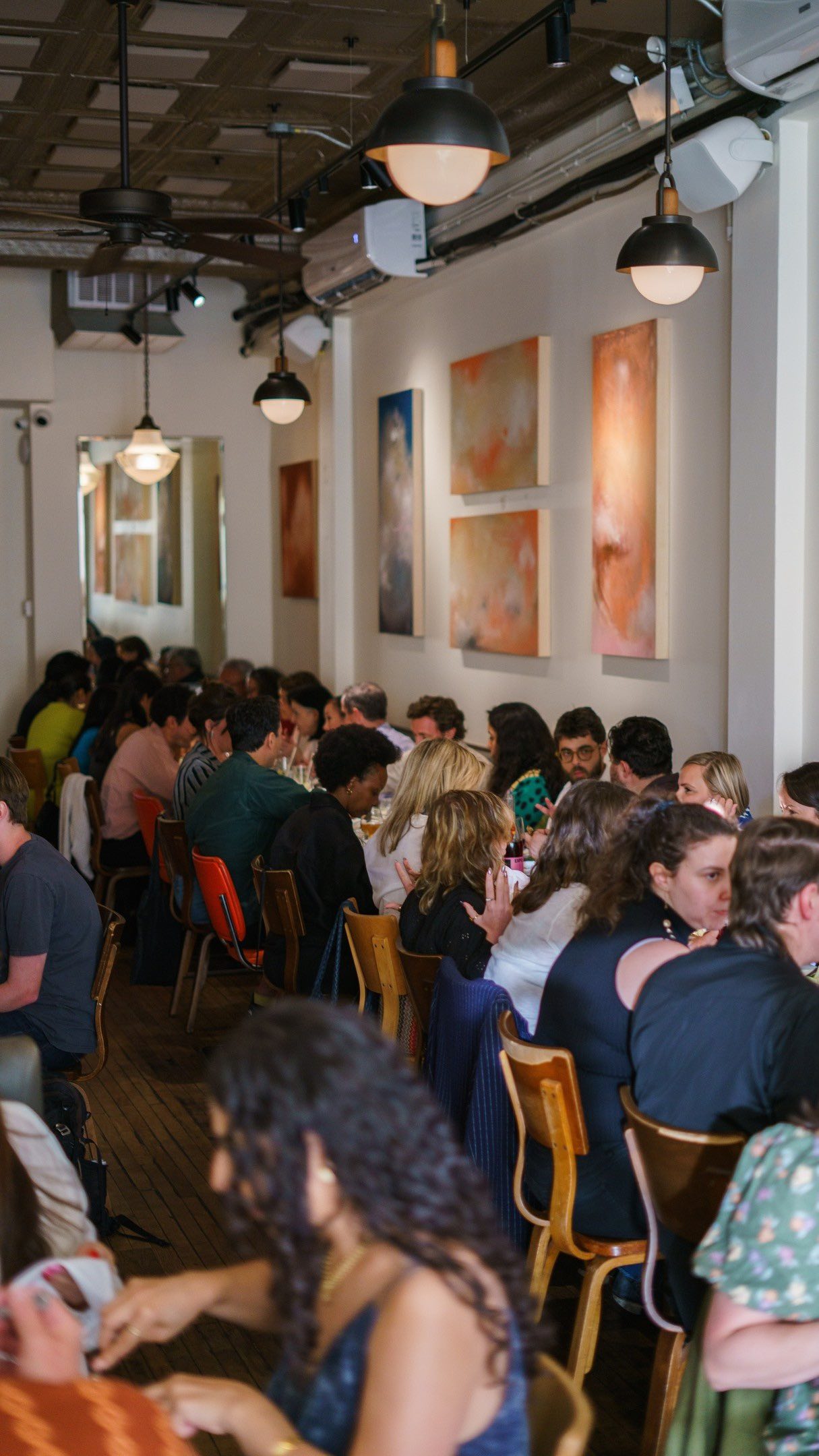 A full dining room of guests seated at long tables during a benefit dinner at Lula Cafe in Logan Square