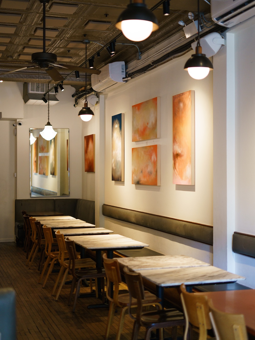 Lula Cafe's long dining room with wooden tables, pendant lights and paintings on white walls