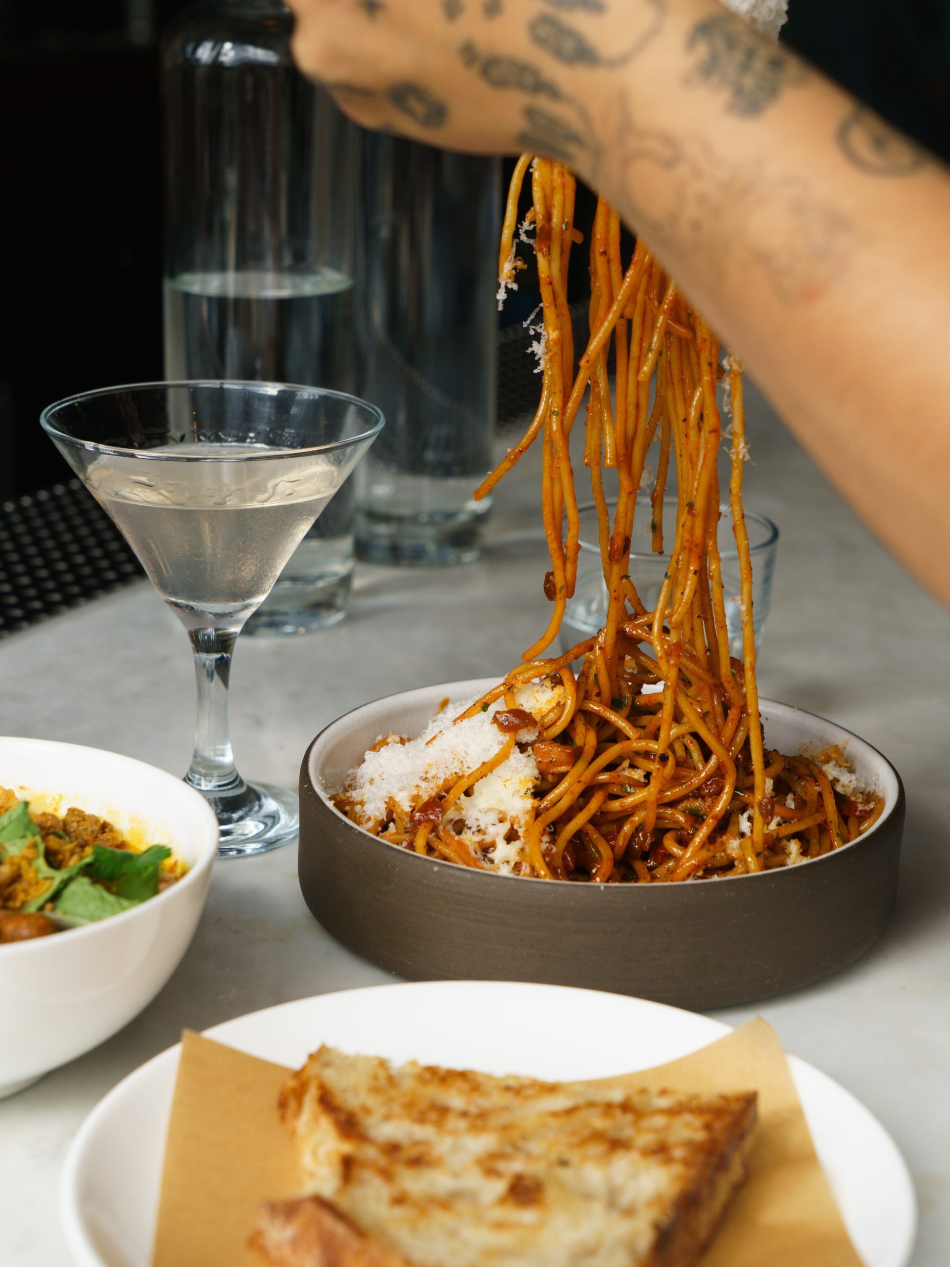 Spaghetti twirled from a bowl beside a martini and grilled bread at the Lula Cafe bar