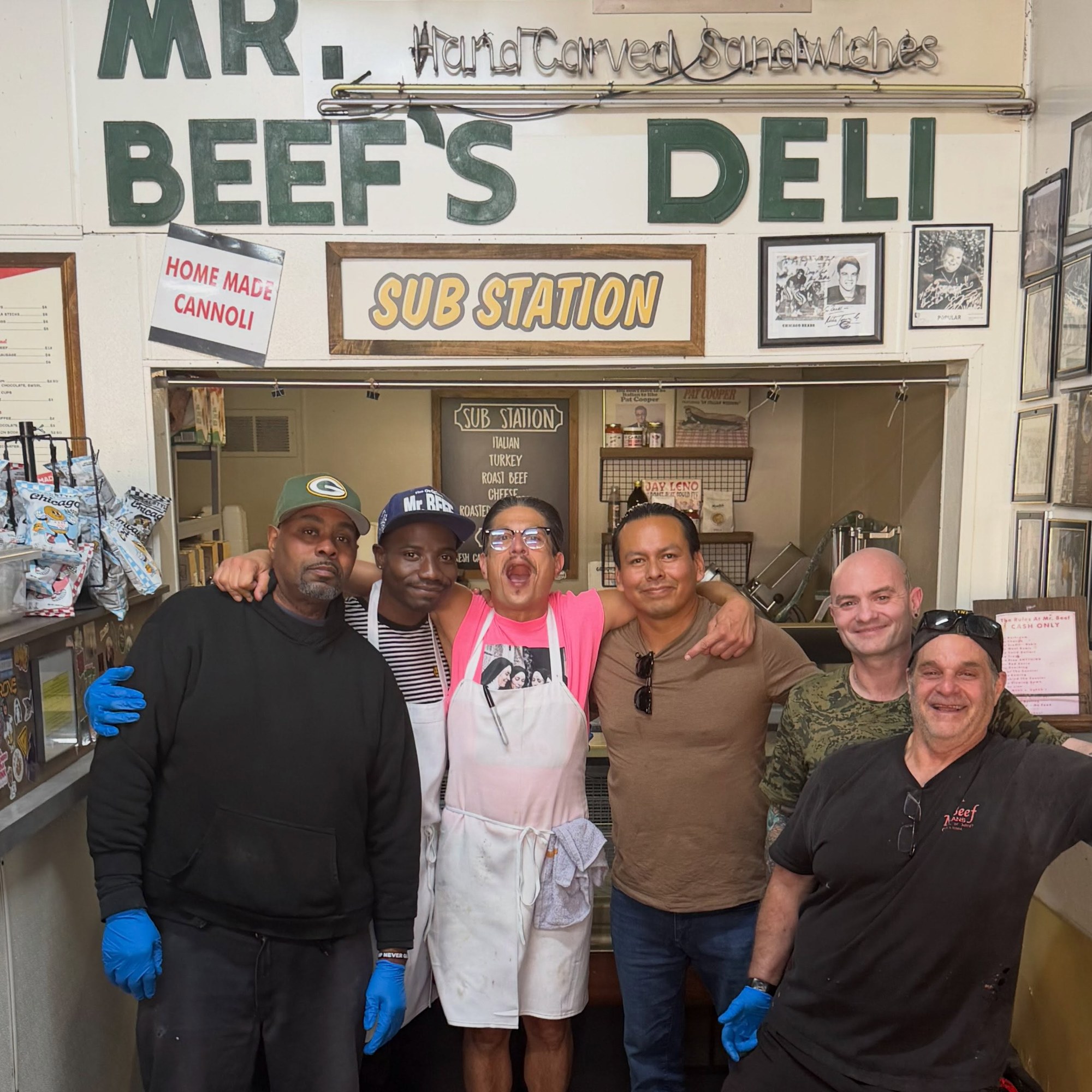 Mr. Beef staff in gloves and aprons posing with a guest under the Mr. Beef's Deli sign at the order window