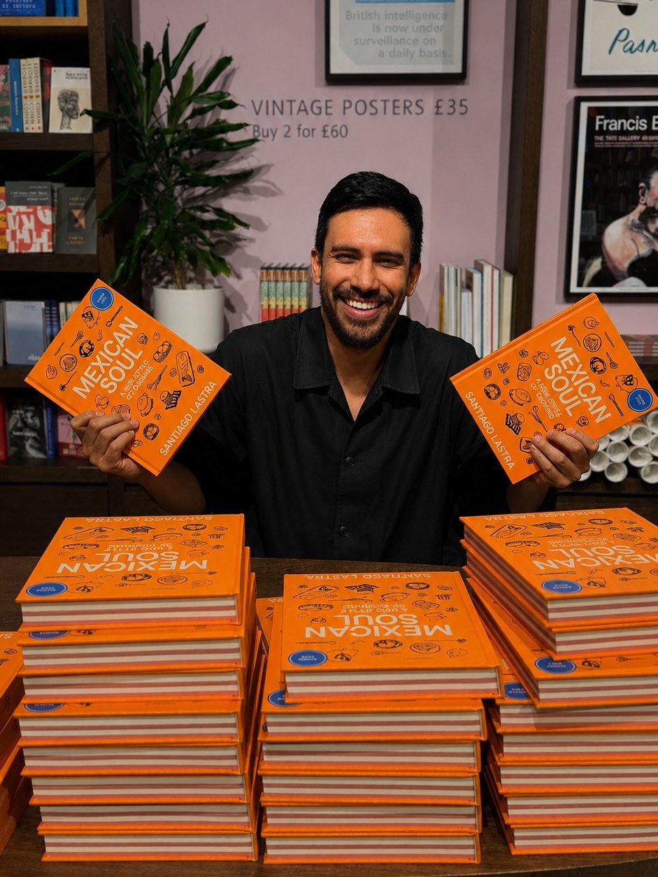 Chef Santiago Lastra smiling behind stacks of orange copies of his cookbook Mexican Soul