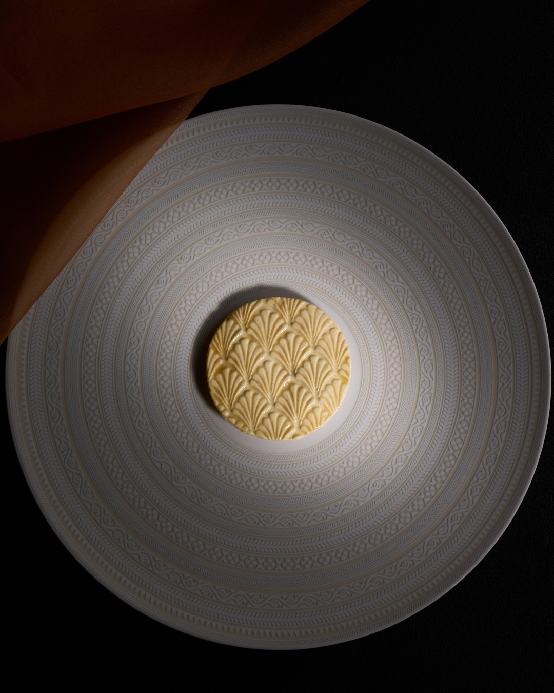 Round sheet of patterned brocade pasta on a white porcelain charger at Next Chicago