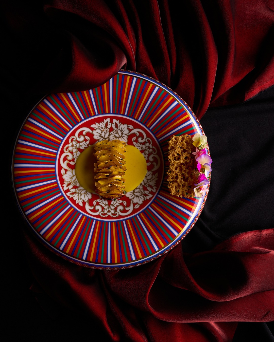 Gathered delicata squash over corn veloute on a red and blue striped plate at Next Chicago