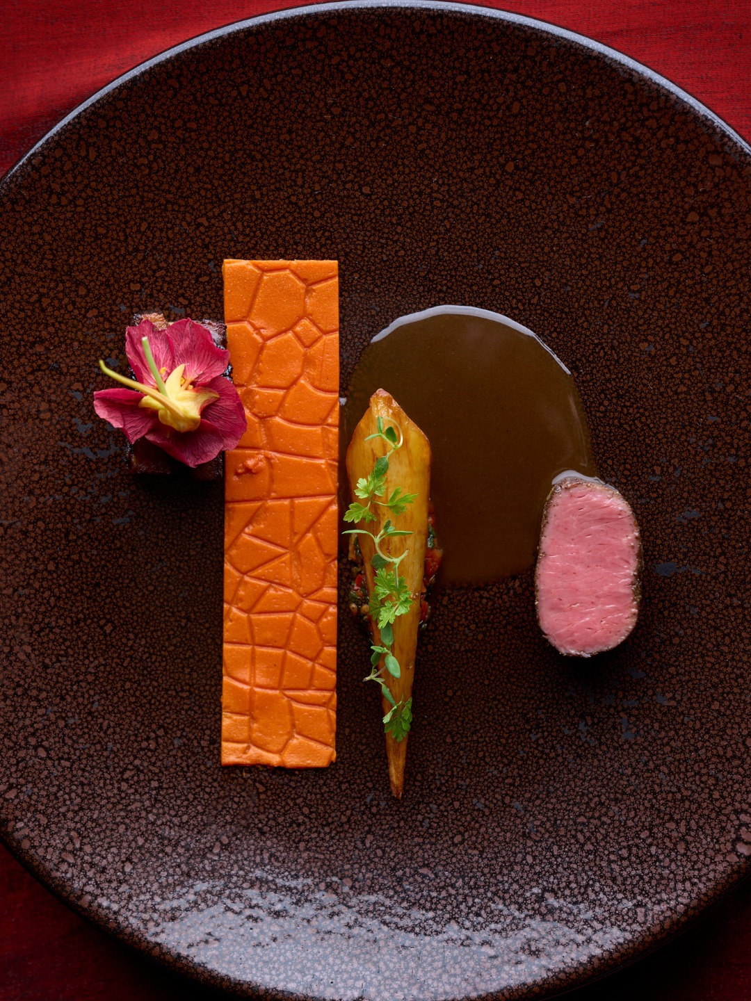 Lamb loin with an embossed orange piquillo pepper panade and glazed parsnip on a dark plate at Next Chicago